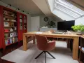Accogliente ufficio in mansarda con scrivania in legno, librerie rosse e lucernario.