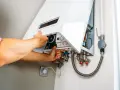 Tecnico che controlla la caldaia, forse per un errore. Si vedono mani che aprono il pannello e tubi.