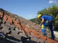 Operaio con imbracatura di sicurezza lavora sul tetto per rifare il tetto, assicurato da cavi e moschettoni.