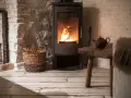 Stufa a pellet moderna con fiamme vive, accanto a un cesto di legna. L'ambiente rustico suggerisce un'installazione a norma, con la necessaria autorizzazione comunale.