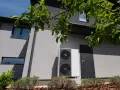 Unità esterna di una pompa di calore, moderna e discreta, installata accanto a una porta su una casa grigia.