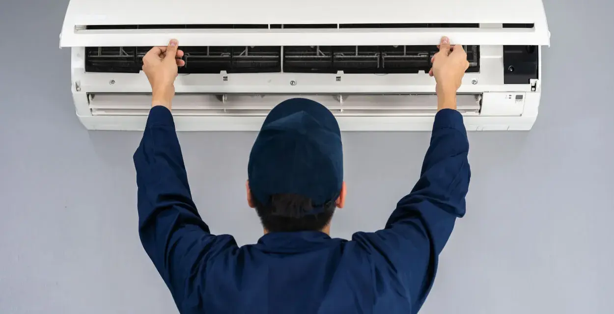 Tecnico con cappellino blu apre il pannello di un climatizzatore per impostare aria fredda.