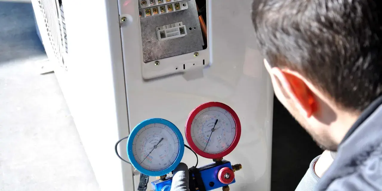 Tecnico controlla i manometri collegati al condizionatore. Se manca il gas nel condizionatore, l'efficienza diminuisce e potrebbe non raffreddare.