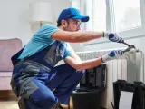 Tecnico con attrezzi effettua manutenzione termosifoni vicino a una finestra.