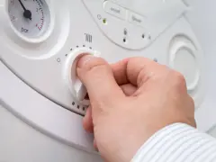 Mano che regola la manopola per impostare la temperatura acqua termosifoni. Si vede un manometro.