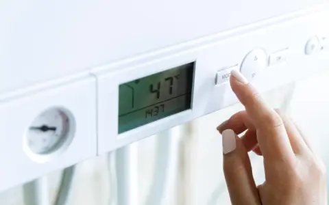 Dito, la mano preme il pulsante "MOD" su una caldaia. Il display mostra 47°C, ma la pressione acqua calda è bassa.