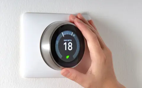 Una mano regola il termostato per impostare la temperatura desiderata, mostrando a cosa serve il termostato: controllare il riscaldamento per il comfort.