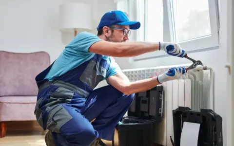 Tecnico con attrezzi effettua manutenzione termosifoni vicino a una finestra.