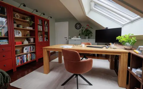 Accogliente ufficio in mansarda con scrivania in legno, librerie rosse e lucernario.