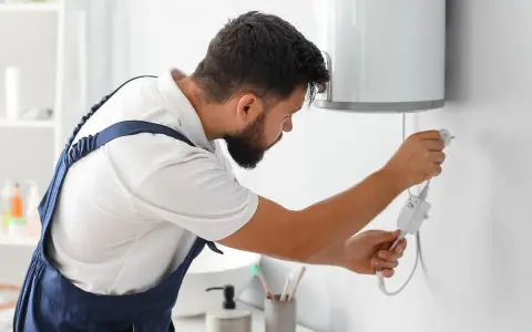 Tecnico con tuta blu controlla la caldaia. La manutenzione caldaia a chi spetta? Al tecnico specializzato, per la sicurezza di tutti.