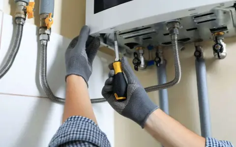 Tecnico con guanti grigi avvita lo scaldabagno. La lancetta scaldabagno cosa indica? Probabilmente la temperatura dell'acqua.