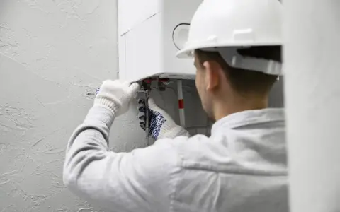 Tecnico con casco bianco lavora su una caldaia. Speriamo che la caldaia non faccia rumore di notte dopo l'intervento.