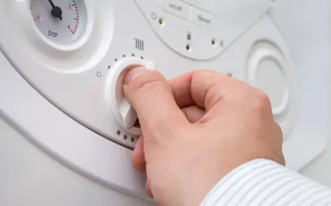 Mano che regola la manopola per impostare la temperatura acqua termosifoni. Si vede un manometro.
