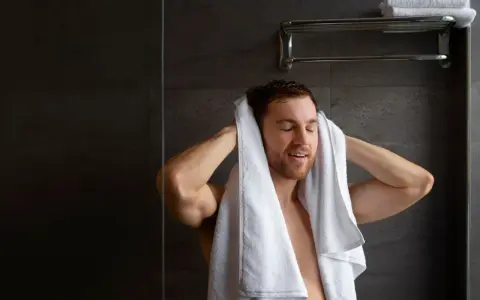 Uomo si asciuga i capelli con un asciugamano bianco. Peccato che non arriva acqua calda solo nella doccia, altrimenti sarebbe stato un bagno perfetto.