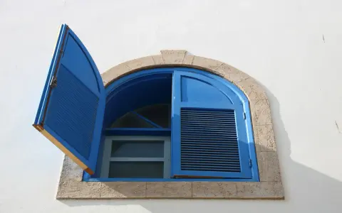 Finestre aperte o chiuse d'estate, con persiane blu su muro bianco. La luce del sole crea ombre nette.
