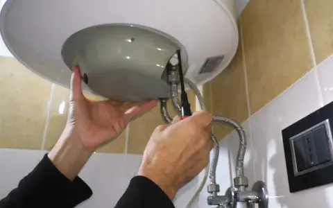 Mani che effettuano la manutenzione dello scaldabagno elettrico, avvitando una vite con un cacciavite.