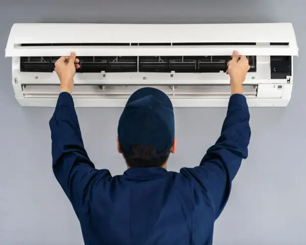 Tecnico con cappellino blu apre il pannello di un climatizzatore per impostare aria fredda.