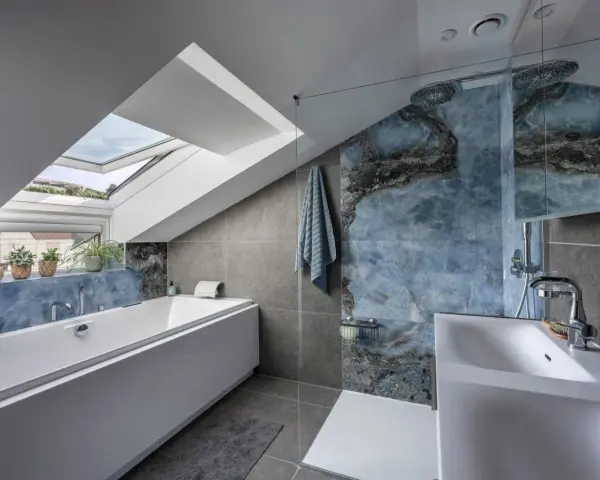 Bagno sottotetto basso con vasca, doccia con piastrelle blu marmorizzate e lucernario.