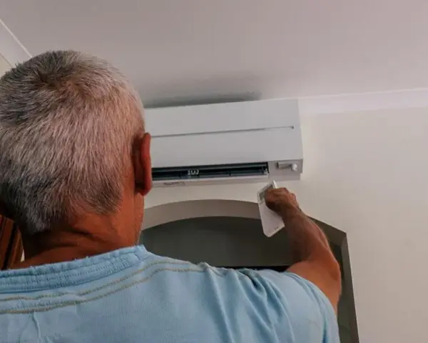 Uomo con telecomando regola il condizionatore per aria fredda, cercando sollievo dall'estate.