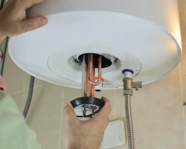 Un tecnico ripara uno scaldabagno che attacca e stacca, mostrando le resistenze in rame.
