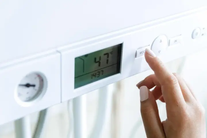 Dito, la mano preme il pulsante "MOD" su una caldaia. Il display mostra 47°C, ma la pressione acqua calda è bassa.