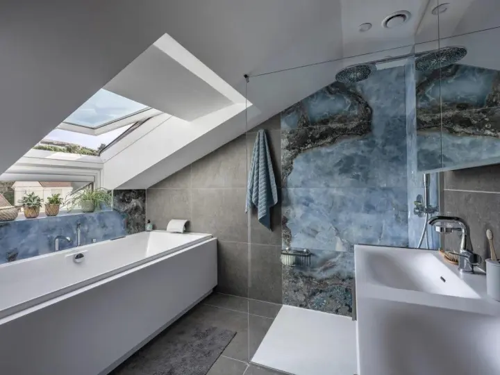 Bagno sottotetto basso con vasca, doccia con piastrelle blu marmorizzate e lucernario.