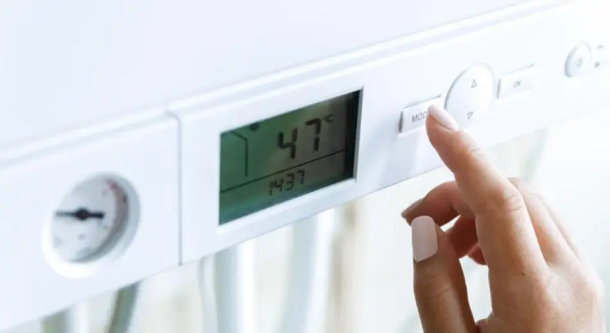 Dito, la mano preme il pulsante "MOD" su una caldaia. Il display mostra 47°C, ma la pressione acqua calda è bassa.