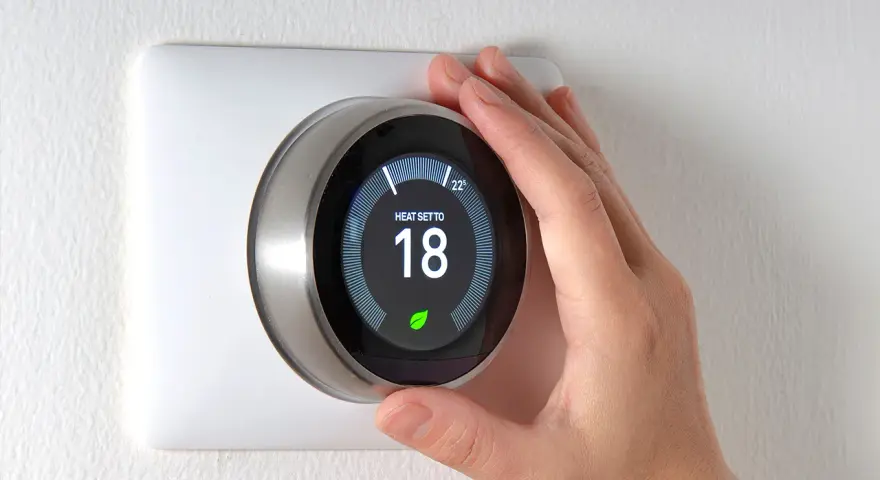 Una mano regola il termostato per impostare la temperatura desiderata, mostrando a cosa serve il termostato: controllare il riscaldamento per il comfort.