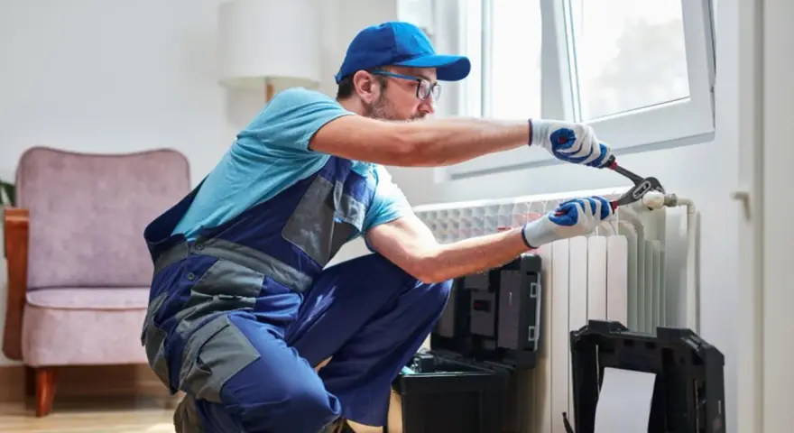 Tecnico con attrezzi effettua manutenzione termosifoni vicino a una finestra.
