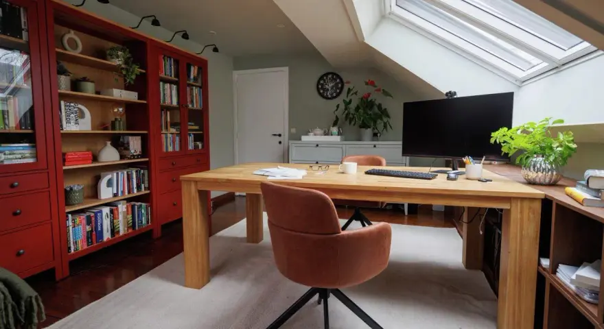 Accogliente ufficio in mansarda con scrivania in legno, librerie rosse e lucernario.