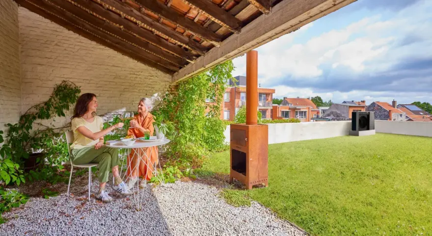 Due donne brindano su un terrazzo con prato. Sullo sfondo, una pompa di calore sul tetto.