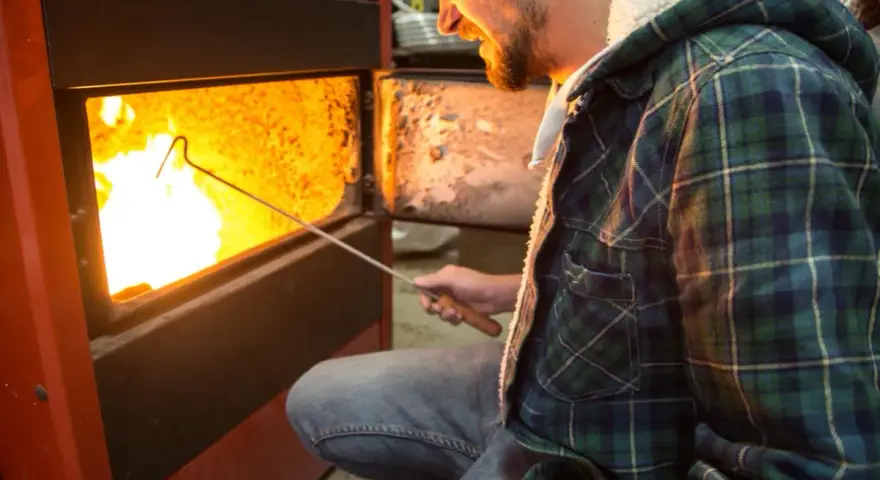 Uomo con camicia a quadri verde accende un fuoco in uno scaldabagno a legna, mostrando come funziona.