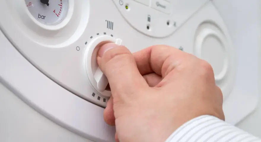 Mano che regola la manopola per impostare la temperatura acqua termosifoni. Si vede un manometro.