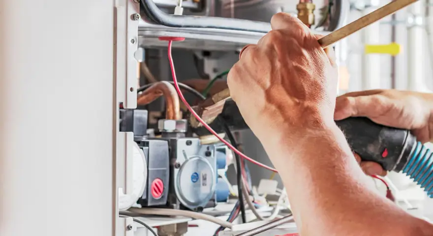 Tecnico che lavora su un **scambiatore acqua calda**, pulendo componenti interni con un pennello e un aspiratore.