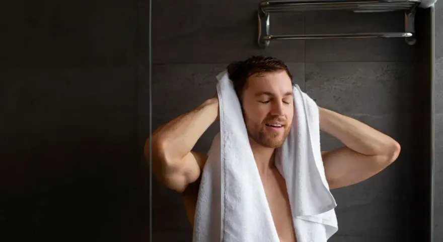 Uomo si asciuga i capelli con un asciugamano bianco. Peccato che non arriva acqua calda solo nella doccia, altrimenti sarebbe stato un bagno perfetto.