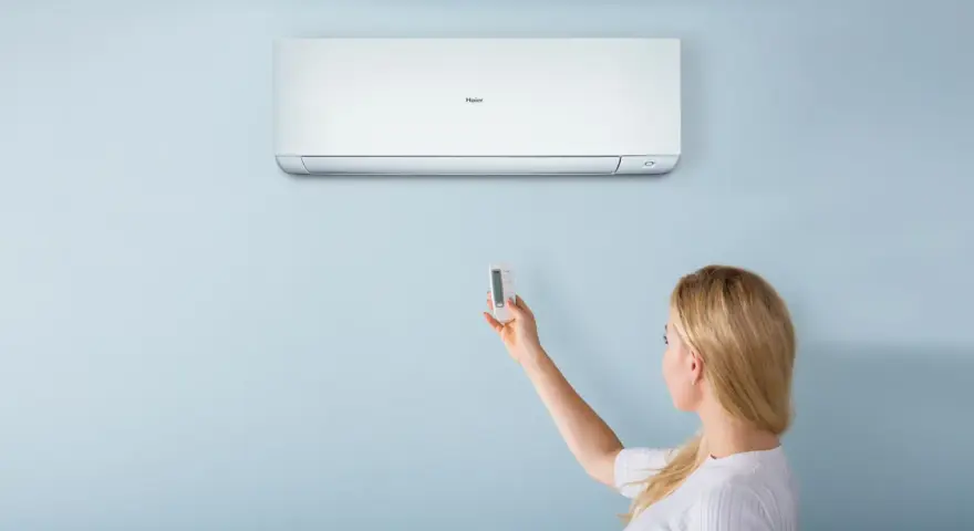 Donna con telecomando regola il condizionatore Haier. Il suo significato è il comfort climatico.
