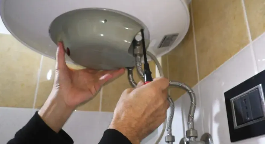 Mani che effettuano la manutenzione dello scaldabagno elettrico, avvitando una vite con un cacciavite.