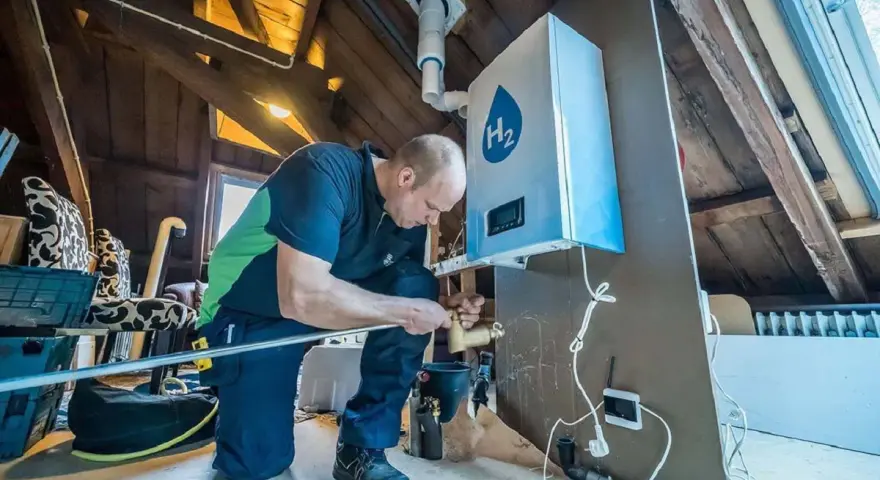 Installazione di caldaie a idrogeno in un sottotetto. Un tecnico collega tubi a un'unità bianca con il simbolo H2.