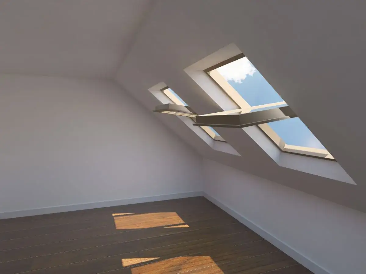 Luce solare entra da una finestra nel tetto, illuminando il pavimento in legno di una stanza vuota.