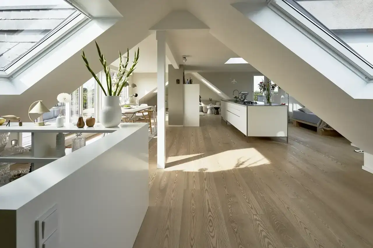 Luminoso sottotetto abitabile con cucina moderna, zona pranzo e letto. Tetti spioventi e lucernari inondano lo spazio di luce naturale.