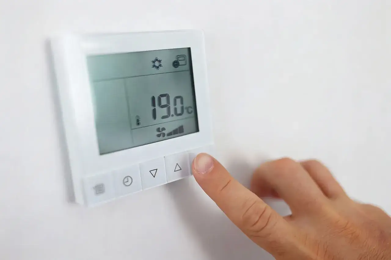 Dito l'indicatore temperatura scaldabagno mostra 19°C, con un dito che preme il pulsante di aumento.